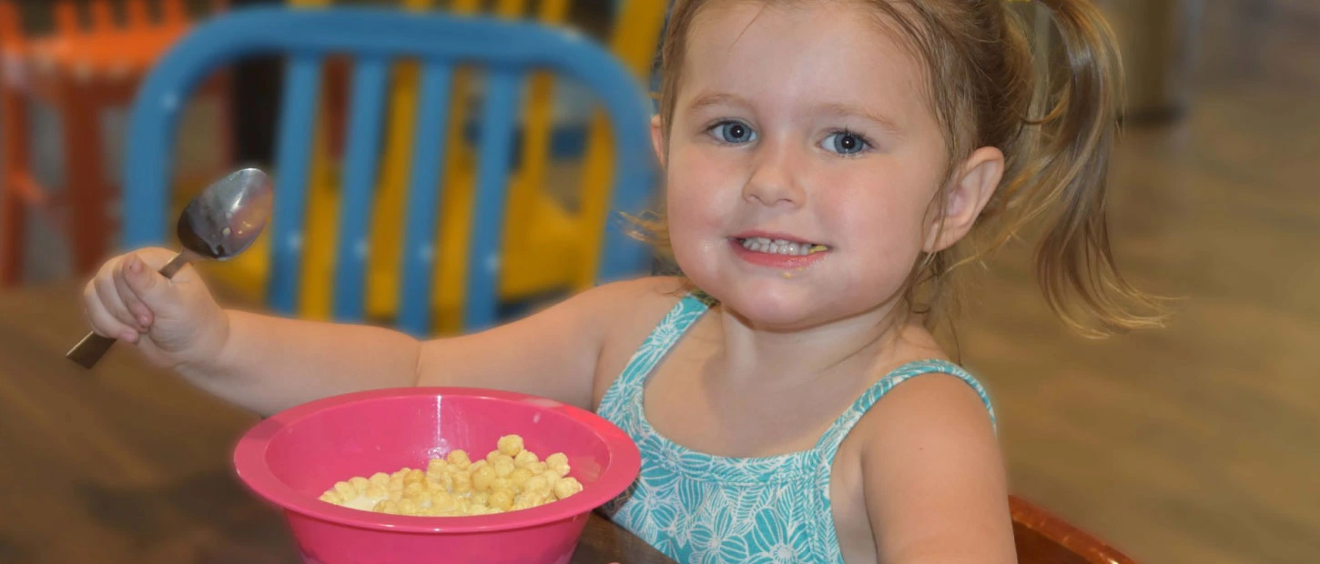 young girl smiling and holding spoon as she eats a bowl of cereal