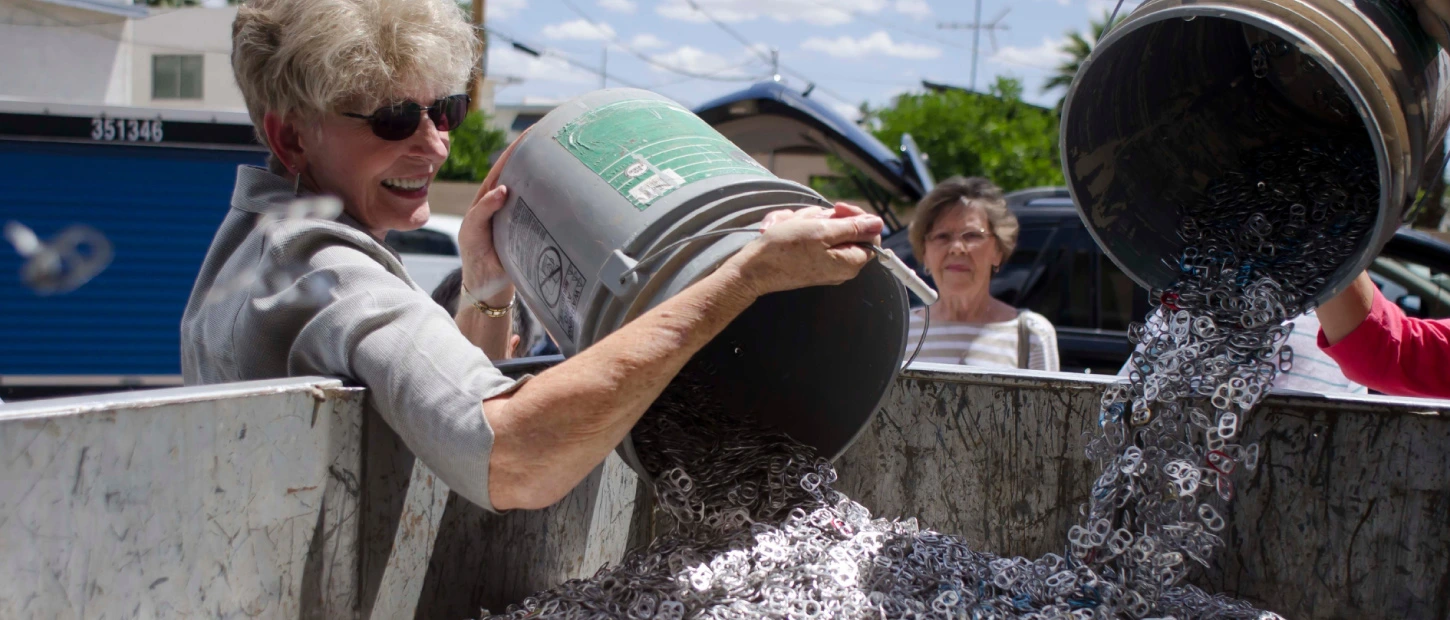 volunteer unloading a five gallon bucket full of soda can pop tabs into collection bin