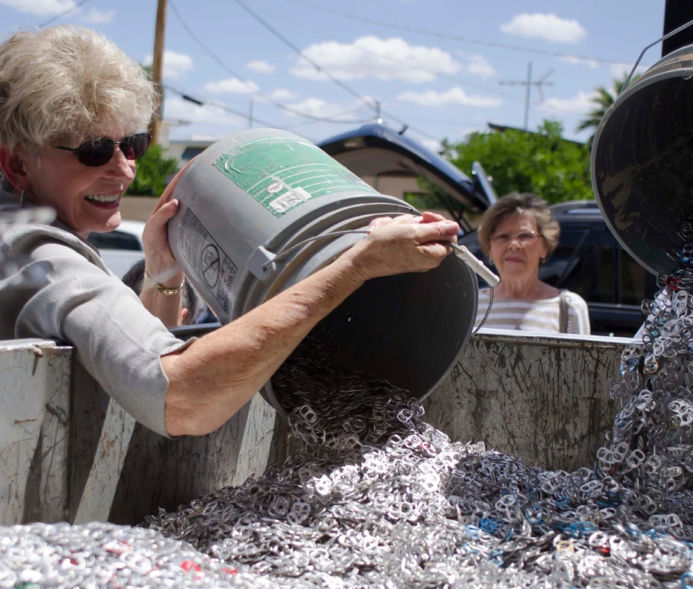 volunteer unloading a five gallon bucket full of soda can pop tabs into collection bin